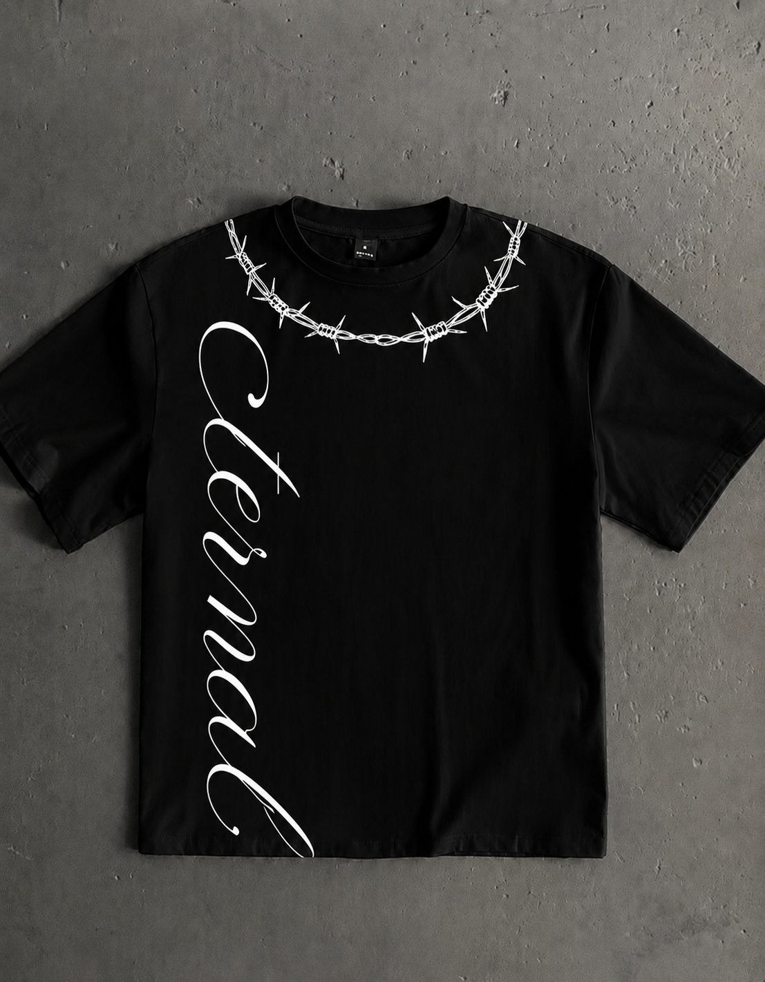 Black oversized Eternal Structure t-shirt with a barbed-wire collar graphic and vertical script, laid on raw concrete